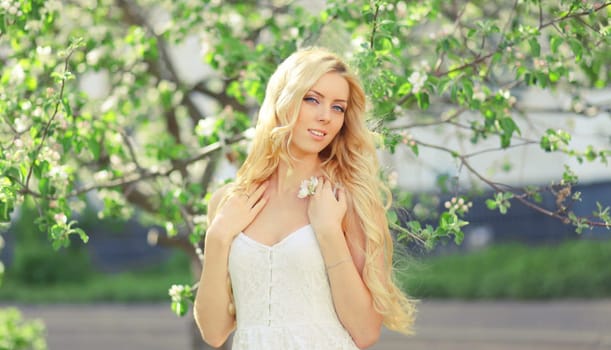 Beautiful young woman with blonde long hair in spring blooming garden on a sunny day against flowers trees background