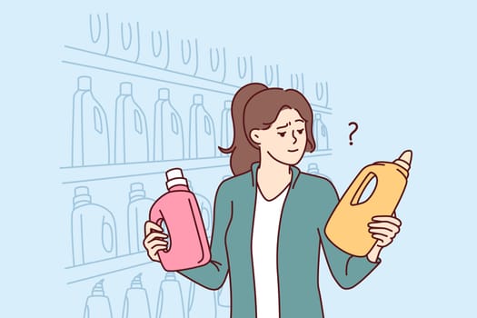 Woman holds bottles of laundry detergent or cleaning product standing near shelves in grocery supermarket. Girl visitor to supermarket compares goods choosing best option for purchase