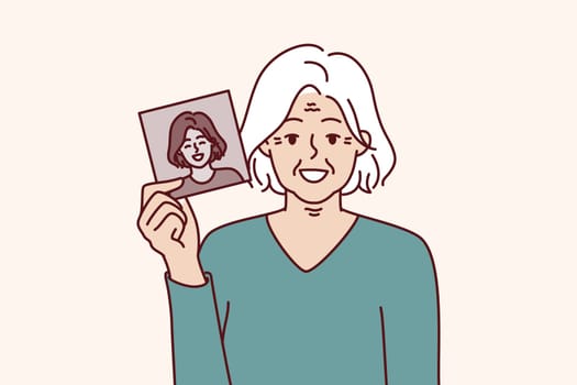 Elderly gray-haired woman shows own old photo for concept of memory of past and nostalgia