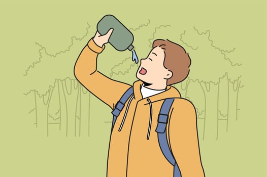 Man drinks water hiking in forest feeling thirsty after long walk through wilderness area with trees. Young guy with flask is fond of hiking and travels in national nature reserve.