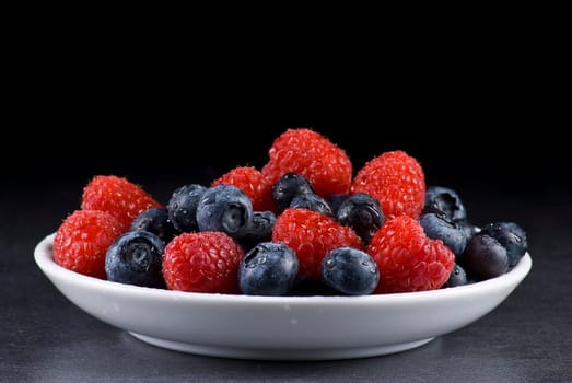 Plate of fresh blueberries and raspberries on balck background