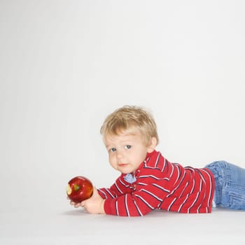 Studio portrait of Caucasian boy holding apple against white background.