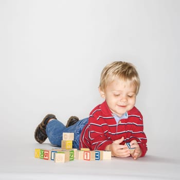Studio portrait of Caucasian boy lying on stomach propped up on elbows playing with toy blocks.