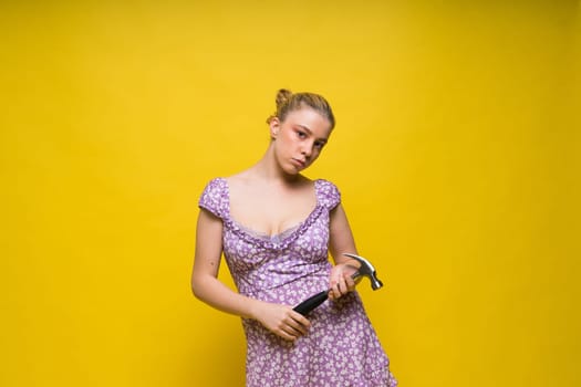 Beautiful seductive female holding hammer, isolated on a yellow and red