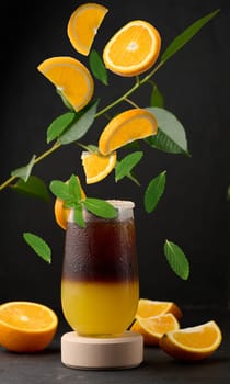 Iced coffee with orange juice in a transparent glass, refreshing bumble coffee on the table. Levitating orange slices and mint leaves