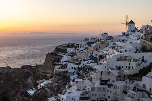 Oia, Santorini, Greece - June 28, 2021: Whitewashed houses and windmills in Oia in warm rays of sunset on Santorini island. Greece