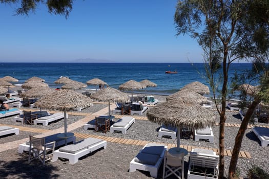 Kamari, Santorini, Greece - June 30, 2021: Sun loungers on the black volcanic beach of Kamari in Santorini. Cyclades, Greece