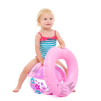 Baby girl in swimsuit with inflatable ring sitting on ball
