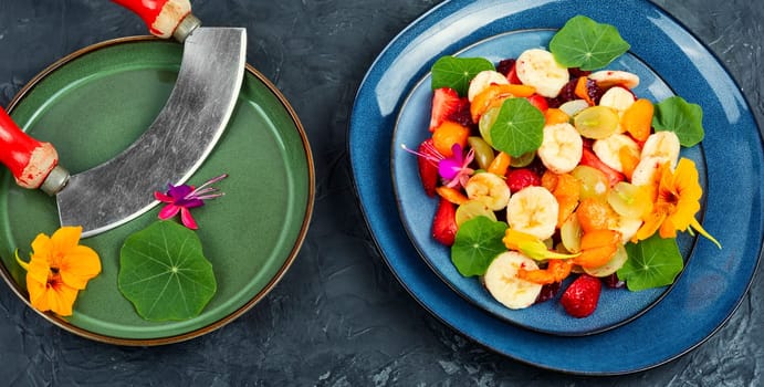 Delicious salad of fresh fruits and nasturtium leaves on grey table.