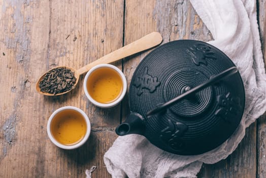 Traditional japanese herbal tea recipe prepared in cast iron teapot with organic dry herbs from above. Top view of asian traditional hot beverage on wooden table.