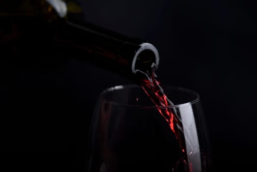 Red wine pouring in wine glass over black background. Closeup of red wine splashing in wineglass in restaurant. Wine tasting.