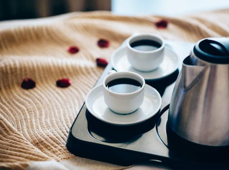 Morning breakfast with black coffee in bedroom. Two cups of coffee on bed decorated with rose petals in luxury hotel bedroom.