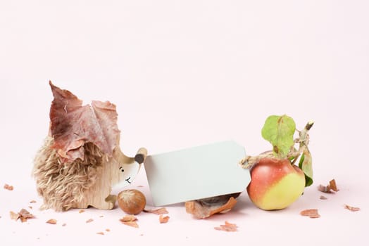 Autumn background with colorful leaves, a blank tag, a hedgehog and an apple, rose colored template and greeting card