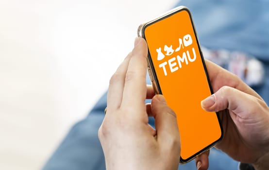 Boston, US, March 2023: Female hands holding a phone with Temu logo displayed on the screen. Temu is an online marketplace. Illustrative editorial