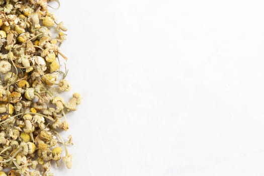 Dried chamomile flowers on marble surface with copy space.