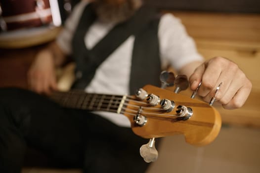 Bearded bald guitarist tuning his musical instrument while sitting on floor. Brutal rockstar rest and preparing for training