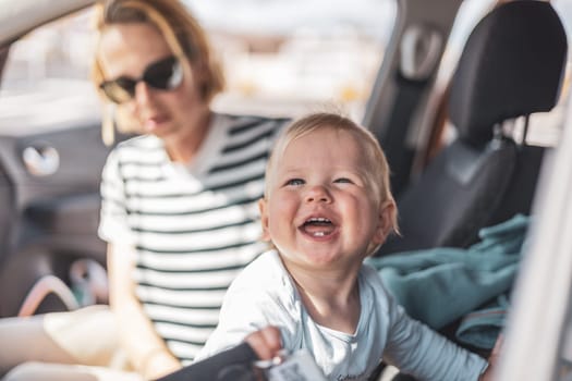 Mother and her infant baby boy child on family summer travel road trip, sitting at dad's front seat, waiting in the car for father to buy farry tickets