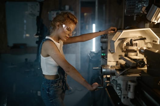 Young blond woman mechanical engineer working on manual lathe machine at motorcycle garage