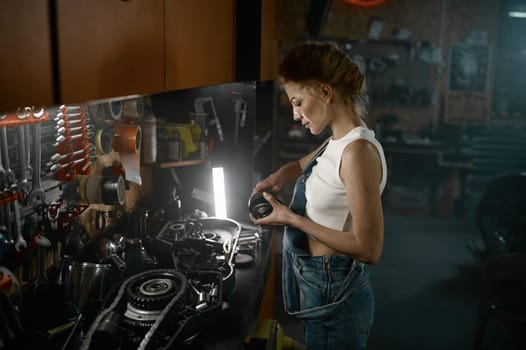 Side view shot of beautiful woman working at workshop garage. Young professional woman technician repairing customer suspension engine system of motorcycle