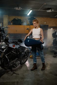Attentive female master fixing fuel tank during repair work with bike at garage workshop