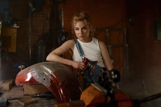 Attractive woman doing hard job at motorcycle garage using grinder to repair some metal bike part