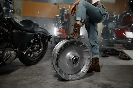 Cropped shot over motorbike garage workshop with female holding leg on chrome wheel disk