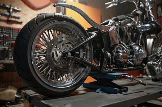 Closeup side view of custom motorcycle placed on lift platform at service station. Sport motorbike maintenance in garage