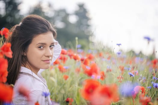 Side view of atractive brunette girl with hand in her hair posing in a red poppies field. Horizontally.