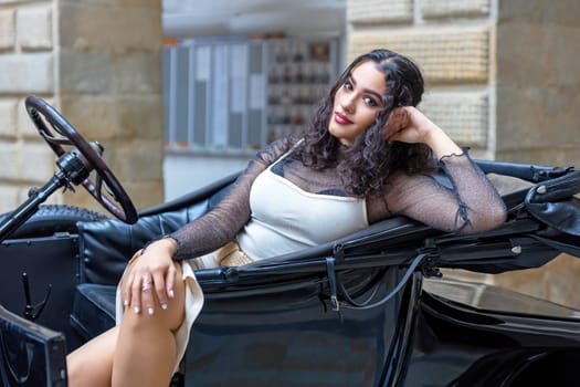 Attractive long black hair girl is resting on vintage car looking at the camera.  Horizontally.