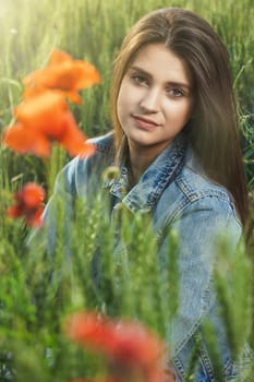 Closeup portrait of beautiful long haired brunette tanned girl dressed in jeans sitting in cornfield.  Vertically.