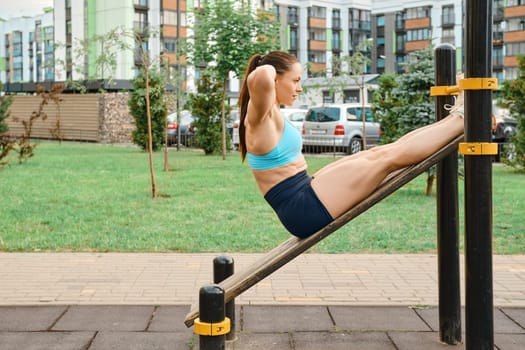 Active woman pumping her abs lying on the sports field of a residential area in the morning