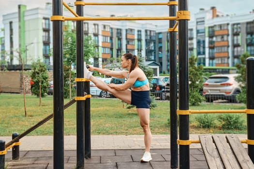 Muscular woman performs stretching for leg muscles outdoors