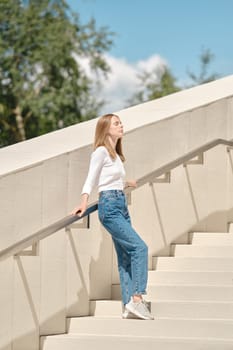 Cute woman standing with her back against railing on stairs and facing the sun