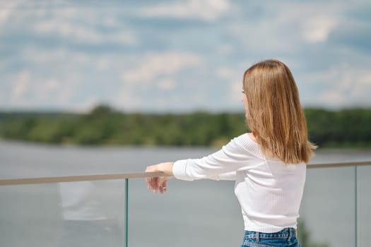 Unrecognizable woman leaning on glass railing on observation deck and looks at water