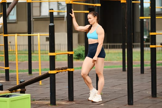 Muscular woman stands near horizontal bar outdoors