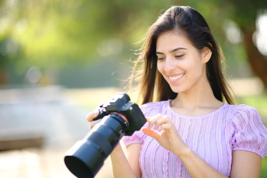 Happy photographer checking photoshoot result on mirrorless porfessional camera in a park