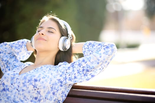 Happy woman listening music resting sitting on bench in a park