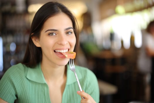 Happy restaurant customer eating tomato looking at camera