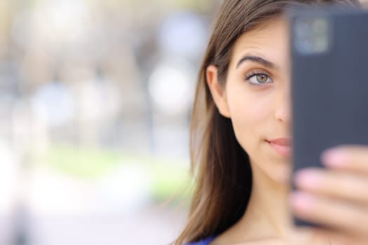 Front view close up portrait of a surprised woman checking cell phone in the street