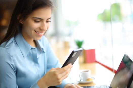 Happy woman using cell phone and tablet in a bar interior
