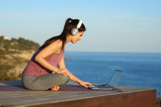 Yogi with headphone and laptop preparing online guided class on the beach