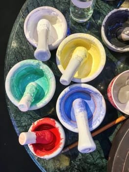 Cups and bowls used as color pots plus well worn brushes standing on a rock table used to paint pottery.