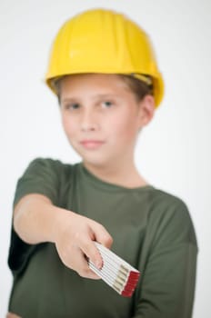 Waist up view of a young teenager wearing a yellow construction helmet and holding a folding ruler in his right hand, pointing at the camera.