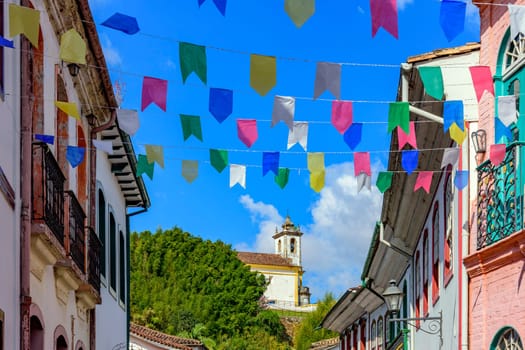 Street decorated with flags for the Saint John festivities with colonial-style houses and a church in the background in the city of Ouro Preto