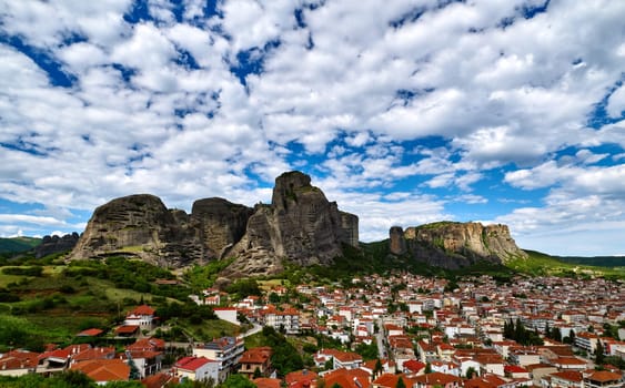 Meteora valley and mountains at day in spring. Blue sky and great clouds over hills and villages of Kalampaka and Kastraki, Greece, UNESCO World Heritage. Famous cliffs and pillars of sedimentary rock. Sun rays travel in patches over ground.