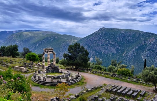 Ruins of Tholos of ancient Greek goddess Athena Pronaia in Delphi, Greece. Three Doric columns with relieves on frieze of circular temple on slope of sacred mount Parnassos and next to famous Delphi complex. UNESCO World heritage site. Wide downshot.