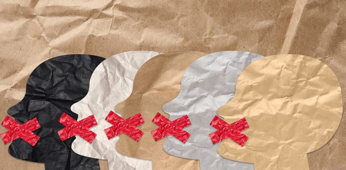 Cutout figures of heads with taped mouths on brown crumpled paper background, lack of freedom of speech concept