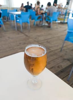 Glass chalice of beer over beach terrace. Spanish chiringuito background