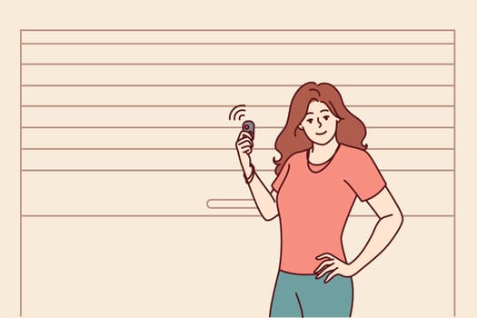 Woman stands near garage door pvc and uses electronic key to automatically open or close entrance. Girl driver poses at garage to securely store own car and protect personal vehicles from theft