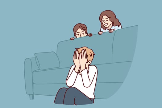 Boy plays hide and seek with friends sitting near sofa and waiting for other children to hide. Three cheerful children spend time together and enjoy weekend or summer school holidays